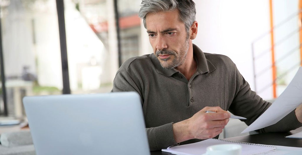 Des mains feuilletant des documents administratifs sur une table en bois, une tasse de café posée à côté